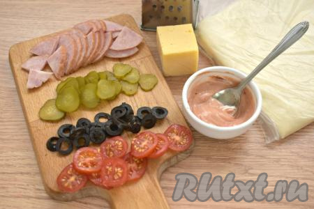 Слоёное тесто заранее достаём из морозилки и оставляем его при комнатной температуре. Тесто должно после разморозки стать мягким. Когда тесто разморозится, можно приступать к приготовлению пиццы. В небольшой ёмкости смешиваем майонез с томатной пастой. Колбасу нарезаем на тонкие ломтики, а затем - на небольшие кусочки. Помидоры и маринованный огурец нарезаем на кружочки, маслины - на колечки.