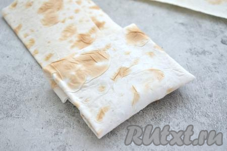 Начинаем сворачивать лаваш с начинкой в форме конверта, для этого сначала загибаем боковые края лаваша на начинку, а затем, начиная со стороны с начинкой, сворачиваем лаваш в форме конвертика. Аналогично формируем ещё 3 таких же конвертика.