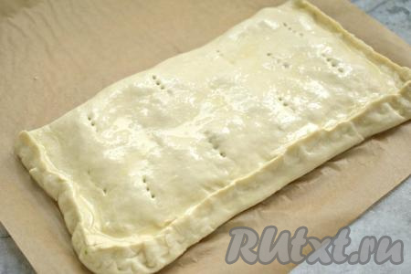 Накрываем тесто с начинкой второй половиной слоёного теста, тщательно скрепляем края. На поверхности пирога делаем проколы вилкой. Смазываем поверхность пирога оставшимся взбитым яйцом.