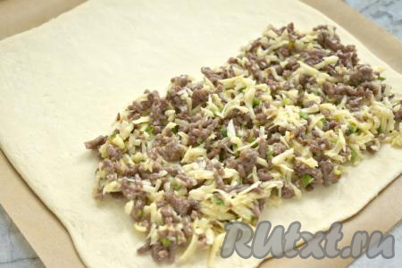 Размороженное тесто на присыпанной мукой поверхности раскатываем в пласт толщиной 3 миллиметра, перекладываем его на противень, застеленный пергаментом. На одну сторону пласта теста выкладываем начинку из фарша и сыра, отступая от краёв теста по 2 сантиметра.