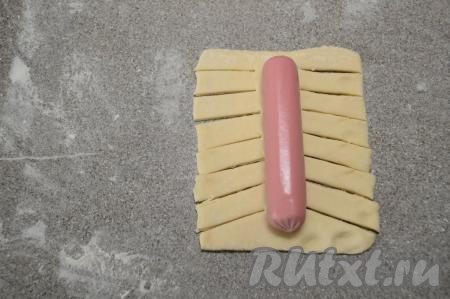 Расположить сосиску в середине раскатанного теста. Острым ножом сделать с двух сторон теста немного косые разрезы, начиная от сосиски и до края теста.