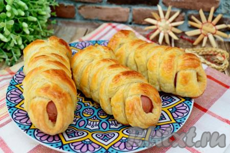 Готовые сосиски, запечённые в слоёном бездрожжевом тесте, достать из духовки. Эту аппетитную, очень вкусную выпечку можно подавать и тёплой, и полностью остывшей. 