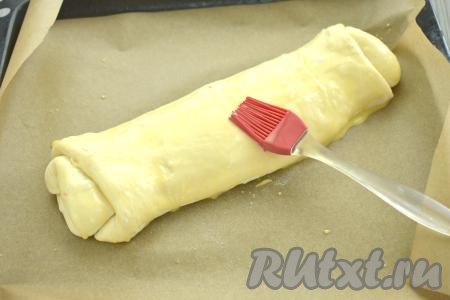 Сворачиваем тесто с начинкой в рулет, начиная со стороны без подгиба. Плотно скрепляем конец рулета. На противень, застеленный пергаментом (или ковриком) для выпечки выкладываем сформированный штрудель швом вниз. Поскольку штрудель формируется из дрожжевого слоёного теста, его нужно оставить на расстойку при комнатной температуре минут на 20 (благодаря расстойке, штрудель станет более воздушным в процессе выпечки).&nbsp;По прошествии 20 минут в небольшой ёмкости взбиваем вилкой яичный желток до однородности. С помощью силиконовой кисточки смазываем поверхность штруделя взбитым яичным желтком.