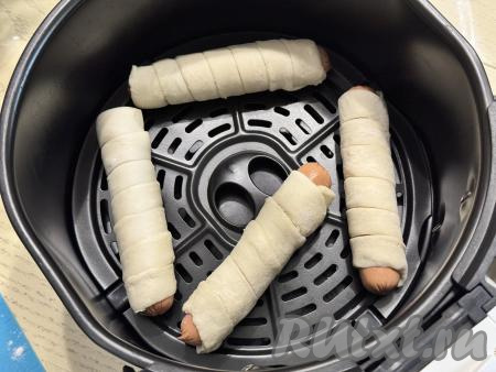 Выложить несколько сосисок в слоёном тесте в чашу аэрогриля прямо на решётку на небольшом расстоянии друг от друга. Выставить температуру 160 градусов, готовить в закрытом аэрогриле 15 минут. Я выпекала по 4 штуки, больше в мою чашу аэрогриля не помещается. 