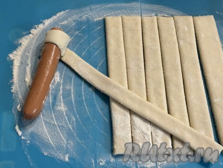 Сосиски очистить от слюды. Обмотать каждую сосиску полоской из теста, начиная наматывать с края сосиски и чуть растягивая полоску из теста.&nbsp;Наматывать полоску из теста на сосиску нужно с небольшим нахлёстом. Край полоски хорошо прижать к тесту.