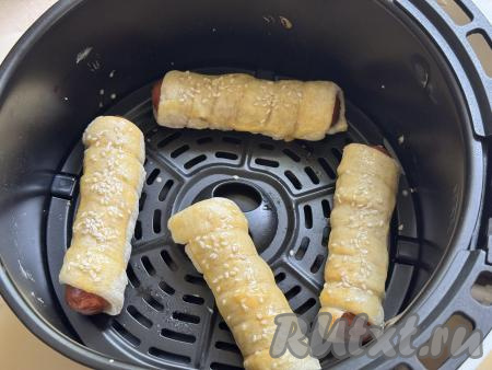 В небольшой ёмкости сырой яичный желток взбить вилкой до однородности. Через 15 минут открыть чашу аэрогриля, с помощью кулинарной кисточки сверху смазать&nbsp;сосиски взбитым желтком, по желанию, можно ещё посыпать сверху кунжутом.