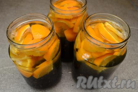 Вскипятить в чайнике воду. Залить банки с чёрной смородиной и апельсинами до самого верха кипящей водой, сразу прикрыть прокипячёнными крышками и оставить постоять минут на 20.