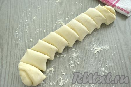 На стол, присыпанный мукой, выкладываем размороженное слоёное тесто, сворачиваем его в рулет, начиная с более широкой стороны пласта теста. Получившийся рулет разрезаем на 8-9 кусочков шириной примерно 2 сантиметра.