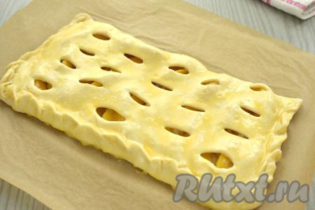 Накрываем начинку из абрикосов стороной теста с надрезами. Плотно скрепляем края теста, формируя бортики пирога. Перекладываем пирог на противень, застеленный бумагой. В небольшой ёмкости яичный желток взбиваем вилкой до однородности. По прошествии 15-20 минут смазываем поверхность пирога с абрикосами взбитым желтком.