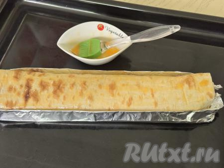 Яичный желток, который откладывался для смазывания рулета, взбить вилкой до однородности. Взбитым желтком смазать поверхность рулета из лаваша.&nbsp;