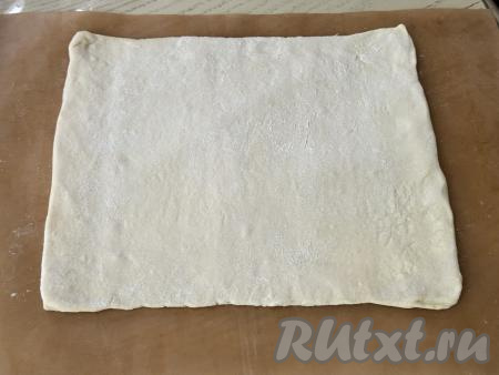На припылённой мукой поверхности один пласт размороженного слоёного теста раскатать в квадрат со стороной примерно 25 сантиметров. Переложить раскатанный пласт теста на противень, застеленный ковриком (или пергаментом) для выпечки.