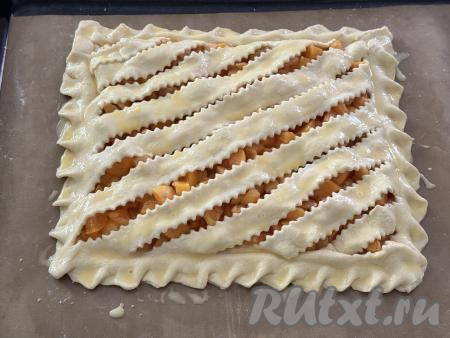 Яичный желток в небольшой ёмкости взболтать вилкой до получения однородной массы. После того как заготовка пирога с абрикосами постоит минут 20-25, смазать верх пирога взбитым желтком. Поставить противень в духовку, разогретую до 200 градусов, выпекать пирог минут 25 (до подрумянивания слоёного дрожжевого теста).