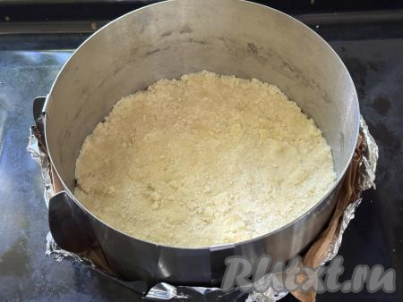 Перетереть руками массу до получения мелкой, однородной крошки. Разделить песочную крошку на две равные части. Разъёмную форму для запекания диаметром 22 сантиметра немного смазать растительным маслом, затем выложить одну часть крошки, равномерно распределить её по дну формы. Слегка утрамбовать крошку. Я в качестве формы для выпечки использовала кулинарное кольцо диаметром 22 сантиметра, сформировав дно из пергамента и фольги, сложенных в 2 слоя. 