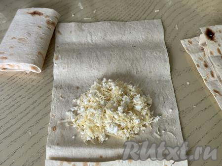 Творожно-сырную начинку тоже разделить на 8 равных частей. Выложить одну часть начинки ближе к одной узкой стороне листа из лаваша, обязательно не забывая отступить от краёв лаваша не менее 2 сантиметров.