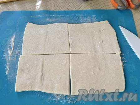 Слоёное тесто у меня было в двух пластах. Вначале на припылённой мукой поверхности раскатать один пласт теста примерно до толщины 3 миллиметра. Раскатанный пласт теста разрезать на 4 части, получатся 4 квадратных заготовки. Второй пласт теста аналогично раскатать и тоже разрезать на 4 части. В результате из двух пластов теста получатся 8 квадратов (то есть мы будем формировать 8 слоек).