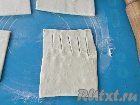 Затем каждый квадрат раскатать в прямоугольник. Зрительно разделить раскатанный прямоугольник на две одинаковых части. На одной узкой части получившегося прямоугольника сделать 4-5 разрезов острым ножом (как на фото), отступая от краёв теста по 1-1,5 сантиметра.