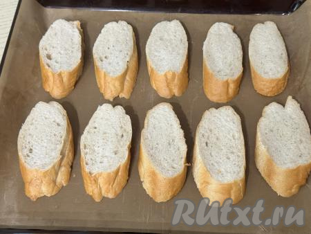 Багет нарезать на кусочки, выложить на противень, застеленный ковриком (или бумагой) для выпечки.&nbsp;