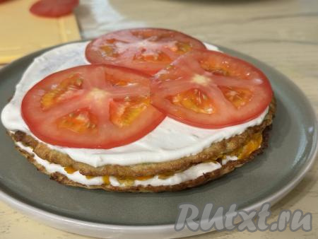 Выложить следующий кабачковый блин, слегка прижать, смазать частью творожно-сметанного соуса,&nbsp;сверху разложить кружочки помидора в один слой, слегка их присолить. Затем выложить следующий кабачковый блин, смазать его частью соуса, выложить ещё 1/3 жареных овощей, таким образом, чередуя слои, собрать весь овощной торт.