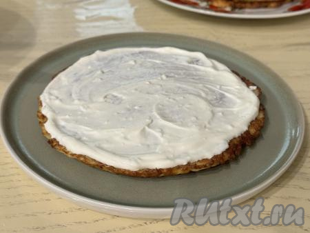 Теперь можно приступать к формированию кабачкового торта. Для этого на плоскую тарелку нужно выложить первый кабачковый блин, смазать его частью соуса из творожного сыра и сметаны.