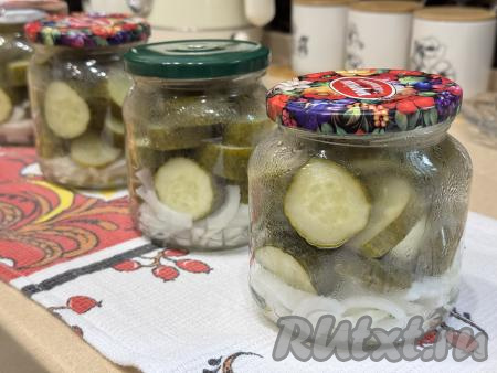 Аккуратно разложить огурцы по банкам. Маринад, который попадёт в банки в процессе раскладывания огурцов слить в кастрюлю с оставшимся в ней маринадом. Прикрыть банки с луком и огурцами прокипячёнными крышками.