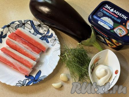 Подготовить продукты для приготовления рулетиков из баклажана с крабовыми палочками. Баклажан помыть, отрезать кончики с двух сторон. Зубчики чеснока очистить. Крабовые палочки разморозить при комнатной температуре.