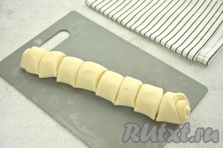 Размороженный пласт слоёного дрожжевого теста, не раскатывая, на присыпанной мукой поверхности сворачиваем в плотный рулет, нарезаем его на 8 кусочков.
