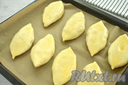 Пирожки из слоёного теста с картошкой выкладываем швом вниз на противень, застеленный пергаментом. Прикрываем полотенцем и оставляем на 20 минут, чтобы слоёное дрожжевое тесто подошло. Затем в небольшой ёмкости яичный желток с молоком взбиваем вилкой до однородности, получившейся смесью смазываем поверхность всех пирожков. 
