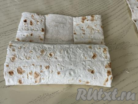 Вначале подвернуть немного два длинных края лаваша на начинку, а затем, начиная с края с начинкой, свернуть лаваш в рулет.