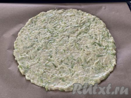 Противень застелить пергаментом, выложить кабачковое тесто на пергамент и сформировать круглую плоскую основу для пиццы диаметром примерно 26 сантиметров. Если не уверены в качестве вашего пергамента, тогда перед выкладыванием теста немного смажьте пергамент растительным маслом. Я предпочитаю брать силиконизированный пергамент, к нему ничего не пристаёт в процессе выпечки.