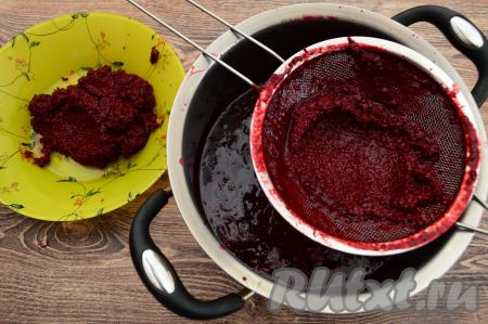 Затем снять кастрюлю с огня, дать ягодному пюре остыть в течение 5 минут. Взять другую кастрюлю с толстым дном, поверх неё поставить сито. Частями выкладывая в сито проварившееся ежевичное пюре, протереть его с помощью столовой ложки через сито. После перетирания очередной порции ежевичного пюре в сите остаются практически сухие косточки, я их перекладываю в тарелку (они нам больше не понадобятся), а в сито вливаю очередную порцию пюре из ягод. В результате в кастрюле будет отделённое от косточек ежевичное пюре. Процедура перетирания не такая уж и долгая, я за 10 минут перетёрла всё пюре через сито обычной столовой ложкой.&nbsp;