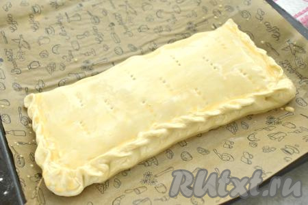 Начинку накрываем свободной стороной теста. Плотно скрепляем края теста, формируя закрытый пирог. На поверхности пирога делаем проколы вилкой. Оставляем пирог на расстойку при комнатной температуре минут на 20. Благодаря расстойке слоёное дрожжевое тесто получится более воздушным. В небольшой миске соединяем яичный желток и молоко, тщательно перемешиваем. По прошествии 20 минут смазываем поверхность пирога смесью желтка и молока.