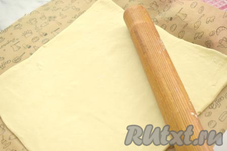 Разморозившееся слоёное тесто выкладываем на стол, припылённый мукой, и раскатываем в квадрат со стороной 29 сантиметров. Раскатанное тесто выкладываем на противень, предварительно застеленный ковриком (или бумагой) для выпечки.