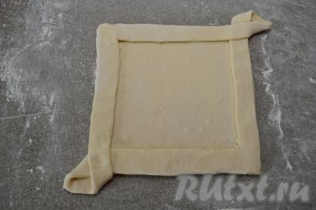 Таким же образом перекинуть второй угол теста с разрезами на противоположный угол, тоже прижать, формируя бортик пирога. Получится квадратная заготовка пирога с бортиками.