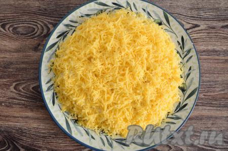 Сыр натереть на мелкой тёрке и разместить следующим слоем, покрывая и верх, и бока салата.