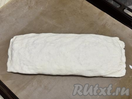Рулет из слоёного теста с сырно-колбасной начинкой переложить на противень, застеленный ковриком (или пергаментом) для выпечки.