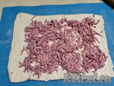 Колбасу натереть на крупной тёрке, затем равномерно выложить на тесто, отступая от краёв теста по 2-3 сантиметра.