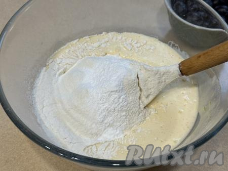 Отмерить муку в отдельную ёмкость, просеять. В миску с масляно-яичной массой всыпать разрыхлитель и половину отмеренной муки, перемешать тесто лопаткой.