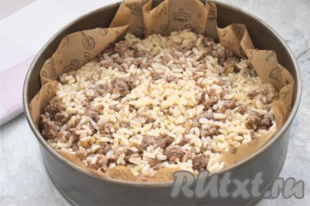 Разъёмную форму для выпечки (я взяла форму диаметром 20 сантиметров) застилаем пергаментом (или просто смазываем дно и бока формы растительным маслом), выливаем половину (или чуть больше) теста, сверху равномерно распределяем остывшую начинку из фарша и риса.