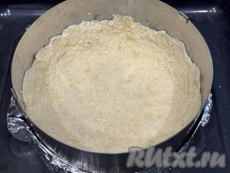 Разделить крошку на две неравные части. Одну часть сделать чуть больше. Выложить большую часть крошки в разъёмную форму диаметром 20 сантиметров и, слегка утрамбовав, сформировать основу для пирога с бортиками. Я в качестве формы для выпечки использовала разъёмное кулинарное кольцо диаметром 20 сантиметров, дно сформировала из пергамента и фольги, сложенной в два слоя. Затем получившуюся форму для выпечки поставила на противень и только после этого выложила большую часть песочной крошки и утрамбовала.