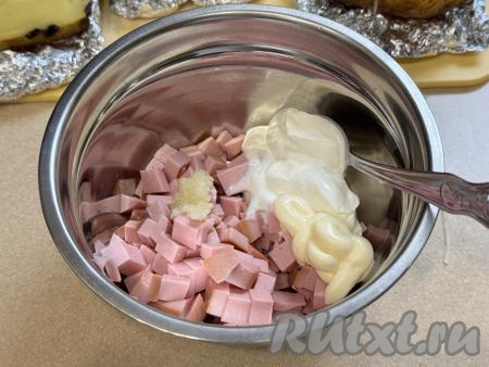Пока картофель запекается в аэрогриле, можно сделать начинку. Колбасу нужно нарезать на мелкие кубики, выложить в миску, добавить пропущенный через пресс чеснок, майонез и сметану, хорошо перемешать, посолить, поперчить по вкусу и начинка для крошки-картошки готова.