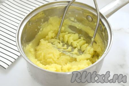 Сварившийся картофель убираем с огня. 50-70 миллилитров отвара, в котором варилась картошка, вливаем в чашку. А затем отвар, который остался в кастрюле с картофелем, выливаем, он нам больше не понадобится. Разминаем картошку толкушкой. В процессе размятия картофеля регулируем густоту пюре, понемногу вливая отвар, который мы оставляли в чашке. Добавляя отвар, учитываем, что картофельное пюре должно получиться в меру плотным, как на фото. Как только добились нужной густоты теста, значит не нужно больше добавлять отвар.