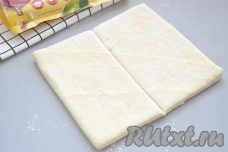 Стол немного посыпаем мукой. Выкладываем на стол размороженную пластину слоёного теста. Раскатывать тесто не нужно. Разрезаем тесто на 2 половинки.