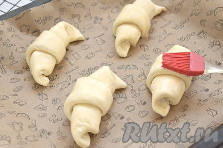 Круассаны&nbsp;на небольшом расстоянии друг от друга  выкладываем на противень, застеленный бумагой для выпечки (круассаны увеличиваются в процессе выпечки). Оставляем круассаны на 20 минут при комнатной температуре, чтобы слоёное дрожжевое тесто немного подошло. Затем в кружке взбиваем сырое яйцо и смазываем им круассаны.