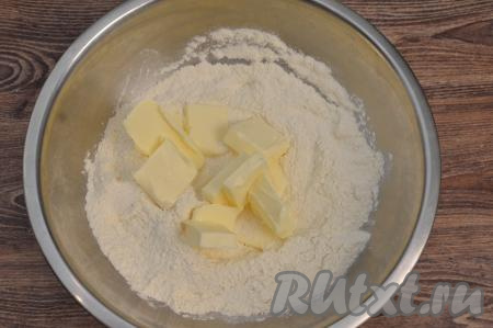В достаточно объёмной миске нужно соединить сухие ингредиенты: муку, сахар, соль, разрыхлитель, перемешать. Достать из холодильника сливочное масло, нарезать его на кусочки, выложить в миску с сухими ингредиентами.