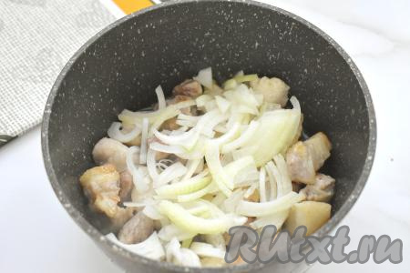 Лук очищаем, нарезаем на четверть кольца, добавляем к обжаренным кусочкам свинины, перемешиваем, обжариваем на среднем огне 3-4 минуты, иногда помешивая.