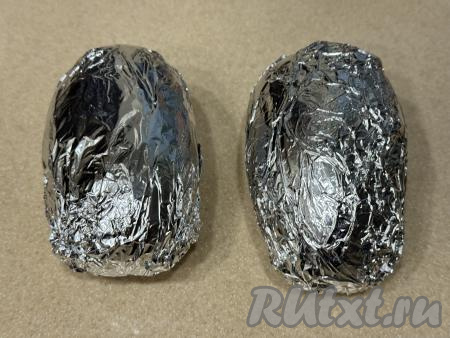 Плотно завернуть каждую картофелину в отдельный лист фольги. Картошку, завёрнутую в фольгу, выложить на противень и поместить в разогретую до 200 градусов духовку, запекать минут 45 (до готовности картофеля). Для того чтобы убедиться в готовности, нужно прямо через фольгу проколоть картошину зубочисткой. Если зубочистка входит в картофель легко, значит картошка готова.