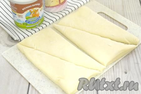 Слегка присыпаем рабочую поверхность мукой, выкладываем размороженный пласт слоёного теста. Раскатывать тесто не нужно. Разрезаем пласт теста по ширине на 2 равные части. Затем каждую половину теста разрезаем по диагонали. В итоге у нас получатся 4 треугольные заготовки для формирования круассанов.