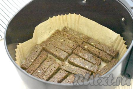 В чашу аэрогриля, предварительно застеленную пергаментом, выкладываем брусочки хлеба так, чтобы сторона хлеба, смазанная чесноком, была сверху.