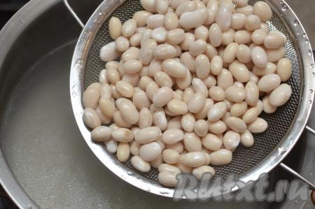 После того как мясо сварится, убрать бульон с огня. Части курицы достать из бульона, оставить остывать. Бульон, если необходимо, процедить, после этого вернуть в кастрюлю и поставить на огонь. Пока бульон закипает, замоченную фасоль выложить в сито, очень хорошо промыть проточной водой, дать лишней жидкости стечь. В закипевший куриный бульон выложить фасоль. Дать бульону с фасолью закипеть, уменьшить огонь. 