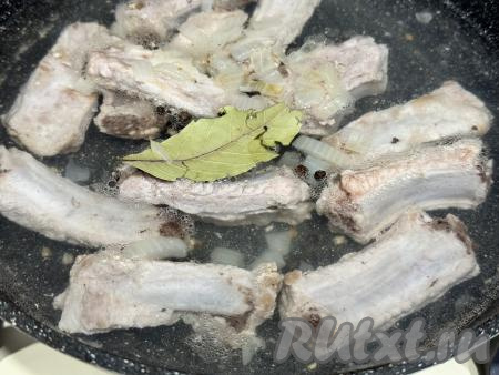 Влить в сковороду 550 миллилитров воды, добавить лавровый лист и горошины чёрного перца. Дать воде закипеть на сильном огне, уменьшить огонь до минимума, накрыть сковороду крышкой, томить рёбрышки 40 минут.&nbsp;Пока тушатся рёбрышки, нужно будет подготовить гречку. Для этого блюда я взяла 210 грамм гречки - это 1 стакан объёмом 250 миллилитров. Гречку, если необходимо, перебрать, удаляя порченые зёрнышки. Гречку выложить в сито, тщательно промыть проточной водой, оставить, чтобы стекла вода, на время, пока готовится мясо.